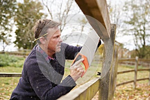 Mature Man Fixing Outdoor Fence With Saw