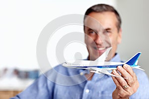 Mature man, flight and toy plane for travel, vacation and holiday planning with a smile at home. Happy, airplane model