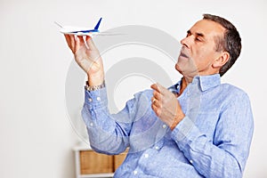 Mature man, flying and toy plane for travel, vacation and holiday planning with a smile at home. Happy, airplane model