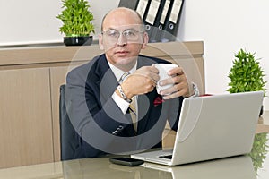 Mature Man in formalwear drinking coffee while sitting at his working place