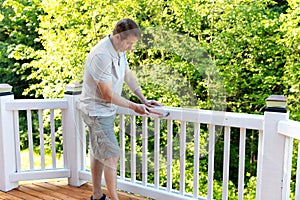 Mature man hammering nail into white railing of outdoor deck