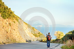 Mature man hiking on mountains nearby sea. Person walking along road. Concepts of adventure, extreme survival, orienteering. Hitch