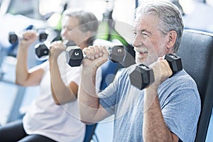 Mature man with his wife doing exercise of biceps at the gym - fitness and healthy lifestyle concept - training their body