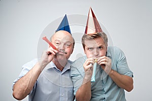 Mature man and his young son celebrating happy birthday wearing funny caps.