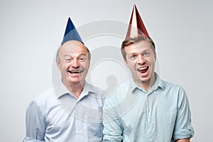 Mature man and his young son celebrating happy birthday wearing funny caps.