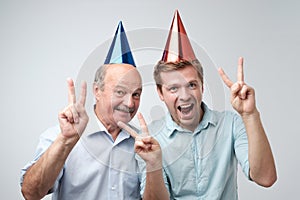 Mature man and his young son celebrating happy birthday wearing funny caps.