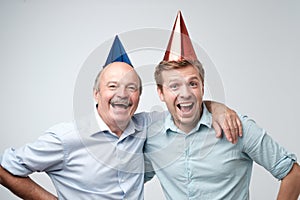 Mature man and his young son celebrating happy birthday wearing funny caps.