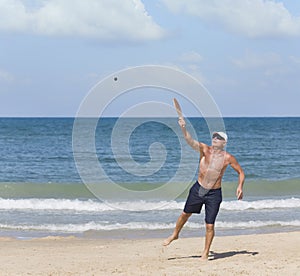 A mature man hits a ball while playing matkot on the beach