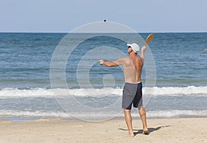 A mature man hits a ball while playing matkot on the beach