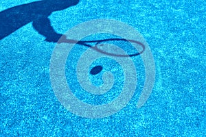 Shadow of mature man hitting tennis ball with racket on blue court