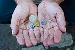 A mature man holding coins in his palms, old age poverty, pension insurance, credit. Ukrainian coins in old hands.