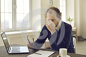 Mature man holding glasses massaging nose feel eye strain after work on laptop