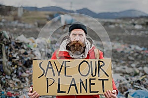 Mature man holding placard poster on landfill, environmental pollution concept.