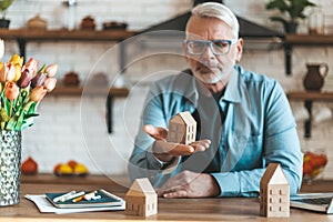 A mature man holds a miniature house in his hands. Loss of money on unprofitable property purchases