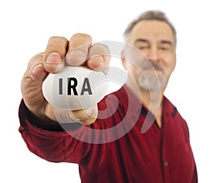 Mature man holds white nest egg with IRA on it.