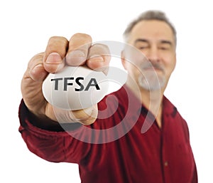 Mature man holds white nest egg with TFSA on it.