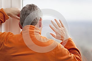 Mature man at home because of covid-19 quarantine looking out of window with raindrops