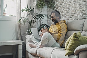 Mature man at home sitting on the sofa doing video call with laptop. Happy and modern male people work on a laptop and wireless