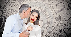 Mature man kissing while giving a red rose to woman