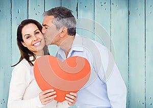 Mature man kissing a woman holding red heart