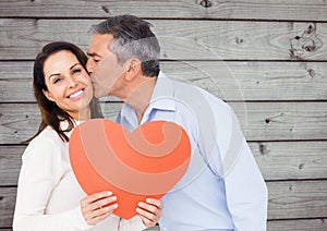 Mature man kissing a woman holding red heart