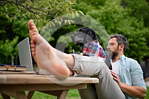 Mature man with laptop and dog working outdoors in garden, home office concept.