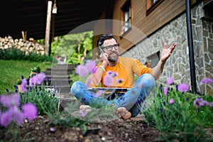 Mature man with laptop and smartphone working outdoors in garden, home office concept.