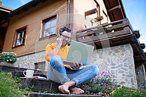 Mature man with laptop and smartphone working outdoors in garden, home office concept.