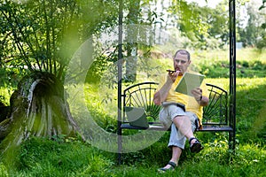 mature man with laptop and smartphone working outside in garden, green home office concept