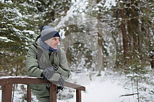 Mature man leaning on wooden railing in snowy winter forest