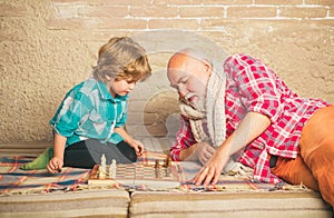 Mature man with little boy playing chess. Checkmate. Cute little boy playing chess. Childhood. Grandfather and grandson