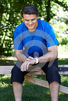 Mature Man Looking At Activity Tracker Whilst Exercising In Countryside