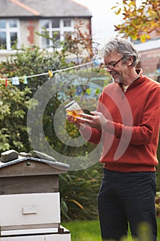 Mature Man Looking At Honey Produced By His Own Bees