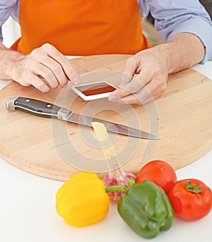 Mature man looking for a recipe of fresh vegetables on the internet on his phone.