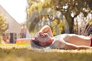 Mature Man Lying On Grass And Sunbathing At Home As Children Play In Pool