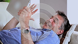 Mature man lying on the sofa using his digital tablet