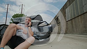 Mature man making a phone call after a car accident, damage car in the background.