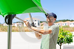 Mature man opening up a green parasol in the garden in a sunny day