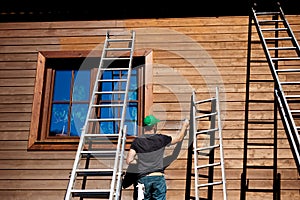 A mature man outdoors in summer, painting wooden house.