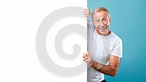 Mature man peeking out blank white advertising billboard at studio