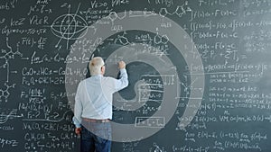 Mature man physicist writing formulas on blackboard with chalk indoors