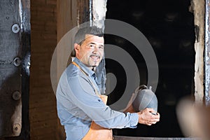 mature man potter holding black glazed ceramic vessel next to kiln