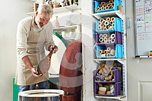 Mature Man In Pottery Studio Firing Vase In Kiln