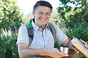 Mature Man Pouring Hot Drink From Flask On Walk