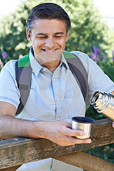 Mature Man Pouring Hot Drink From Flask On Walk