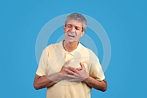 Mature man presses hands to chest expressing pain, blue background