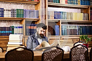 Mature man or professor with long beard and calm face. Historian sits in library and reads old books.