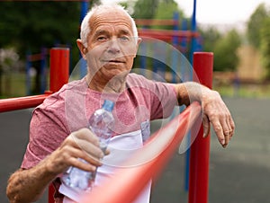 Mature man quenches her thirst from bottle after jogging in park