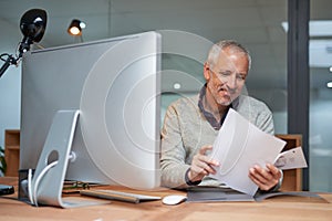 Mature man, reading and documents with computer in office, table and smile for report of sales and profit. Company