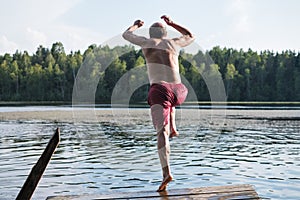Mature man in red swimming clothes jumping into lake.